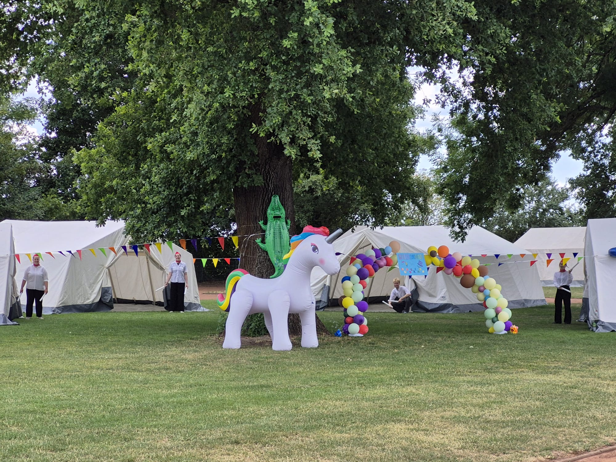 Aufgebaute Zelte auf einer Wiese. Im Vordergrund steht ein aufblasbares Einhorn.